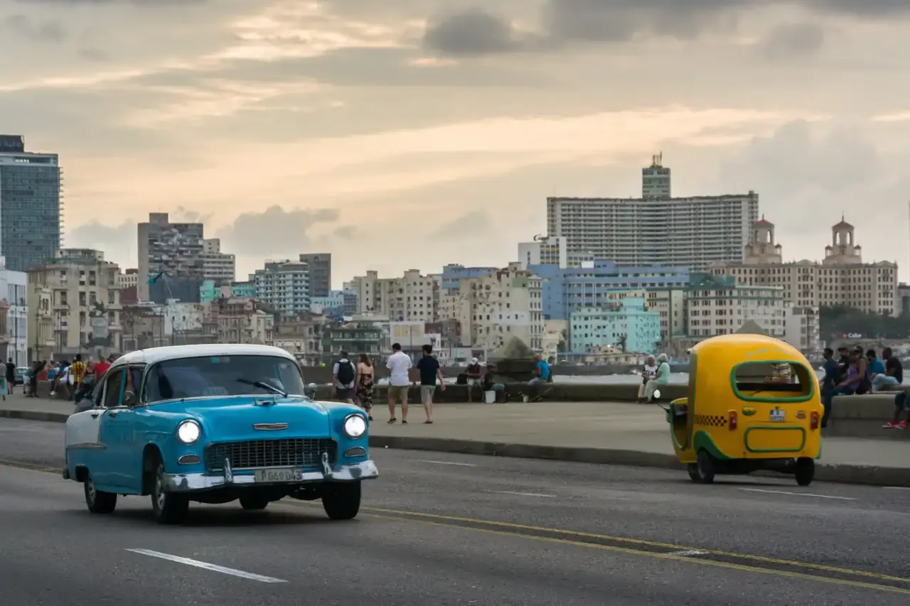 A turquoise classic convertible cruising Havana's Malecón at dusk, past the city skyline