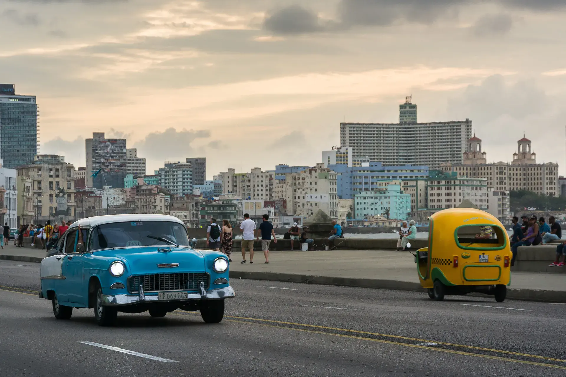 A turquoise classic convertible cruising Havana's Malecón at dusk