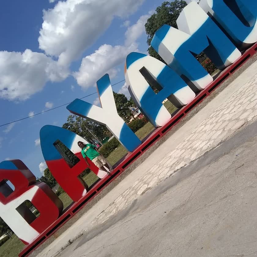 Yoyo leaning against the giant BAYAMO city letters, painted blue, white and red like the Cuban flag, 2019